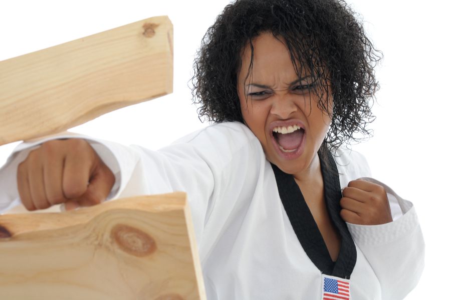 A young woman punching through a wood plank