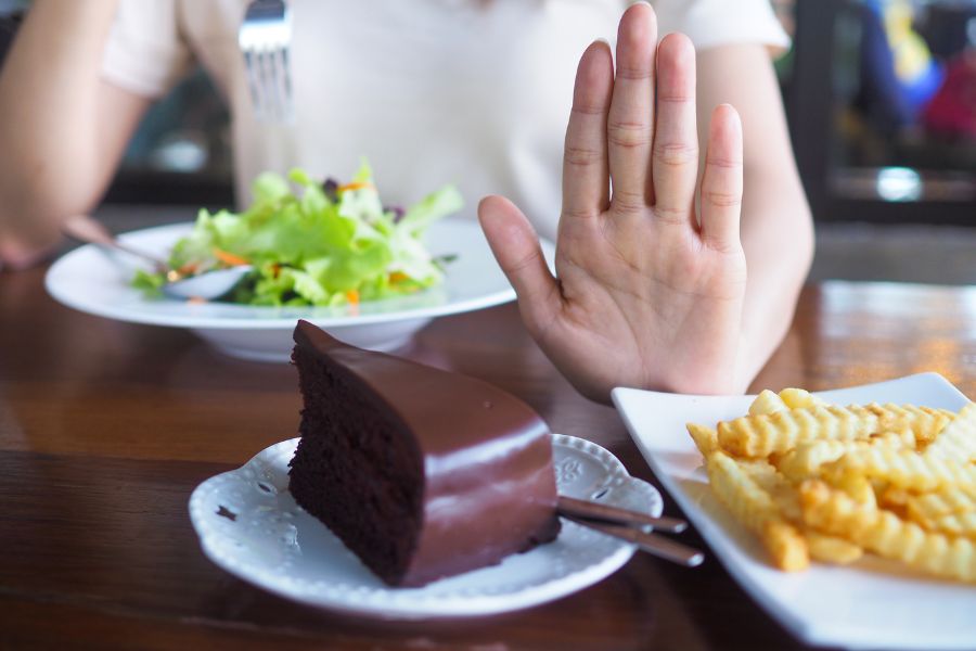 someone eating a salad with their hand up to chocolate cake and fries