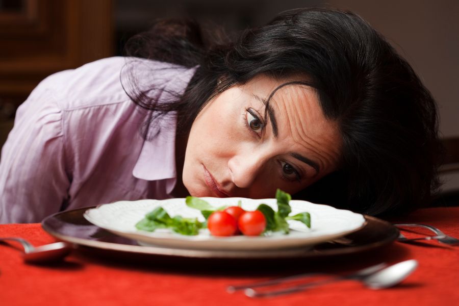a woman staring blankly at a bland salad on a plate