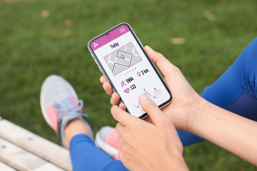 Close-up of smartphone screen showing step counter app with progress graph, hand holding phone while walking outdoors.