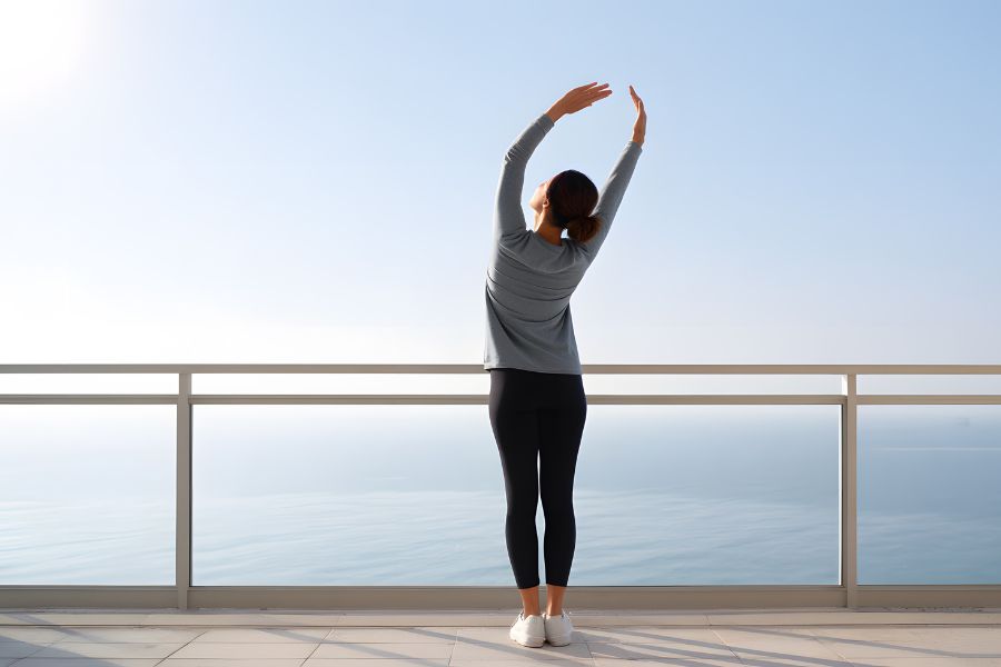 Woman stretching arms toward sunrise on a quiet balcony
